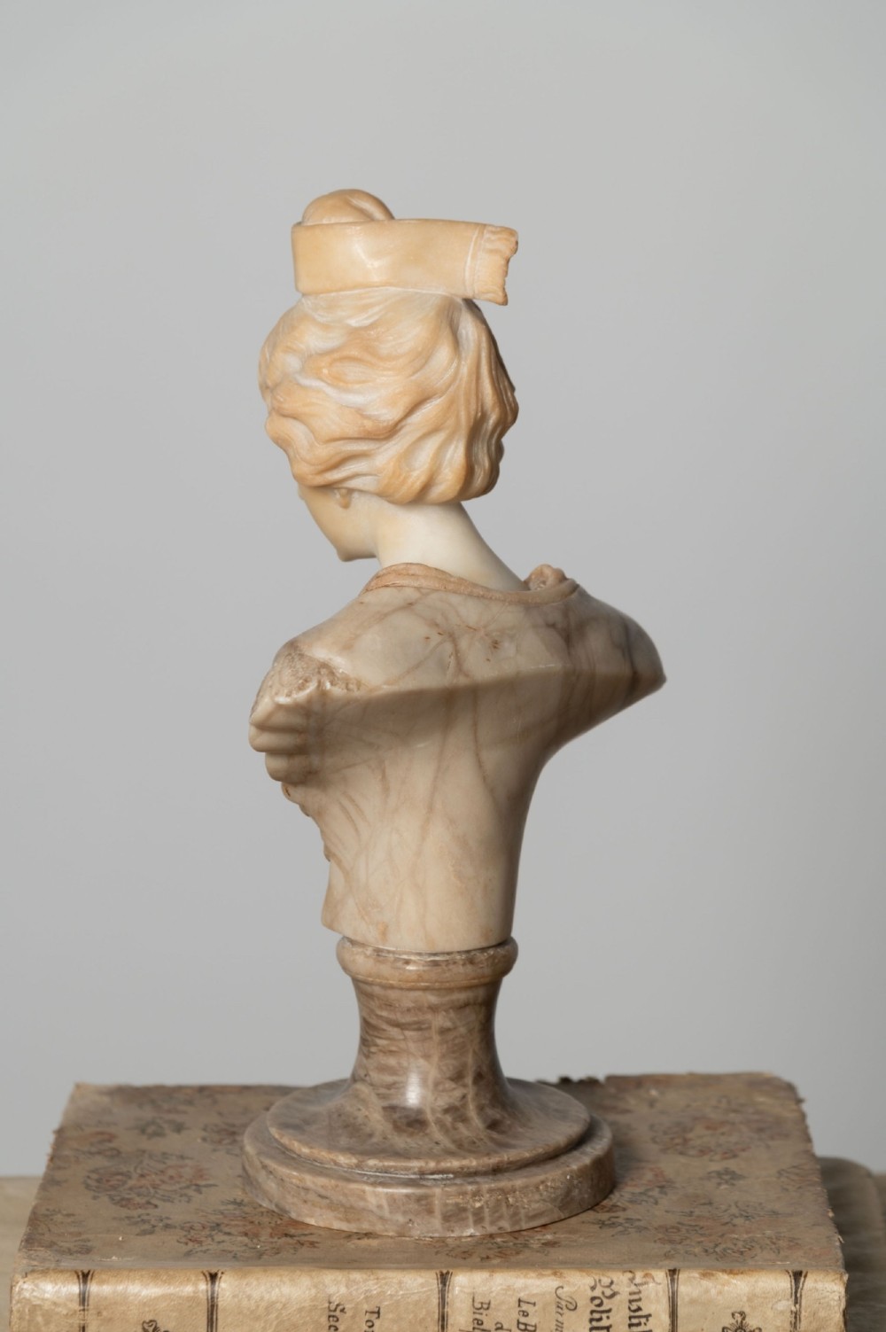 A carved cream alabaster bust depicting a female figure with stylized hair atop a polished turned stone socle. View VI