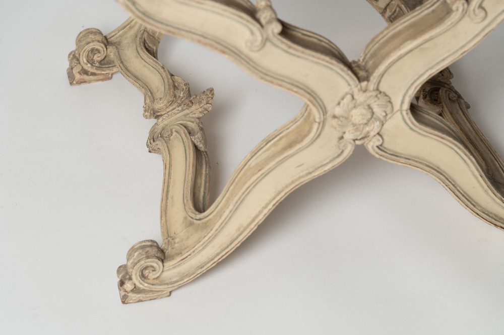 An antique French X-frame stool featuring a painted cream carved wooden base with rosette detailing and a neutral linen upholstered cushion. View II