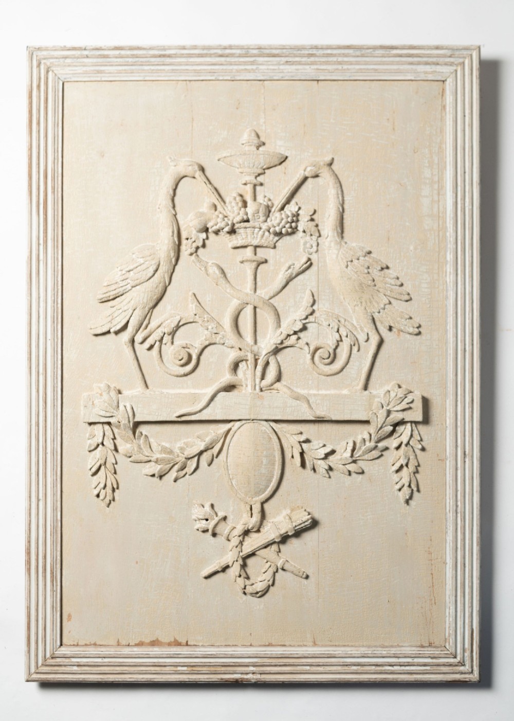 A rectangular off-white painted wood panel featuring an intricate raised relief carving of heraldic cranes, a fruit-filled urn, caduceus serpents, and laurel swags within a moulded frame.