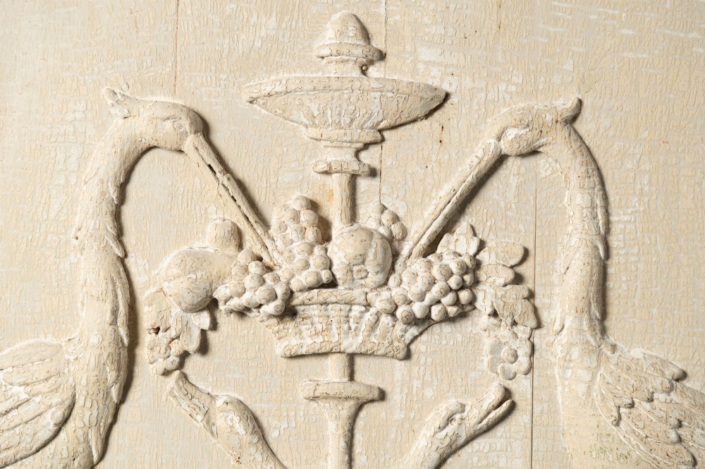 A rectangular off-white painted wood panel featuring an intricate raised relief carving of heraldic cranes, a fruit-filled urn, caduceus serpents, and laurel swags within a moulded frame. View II