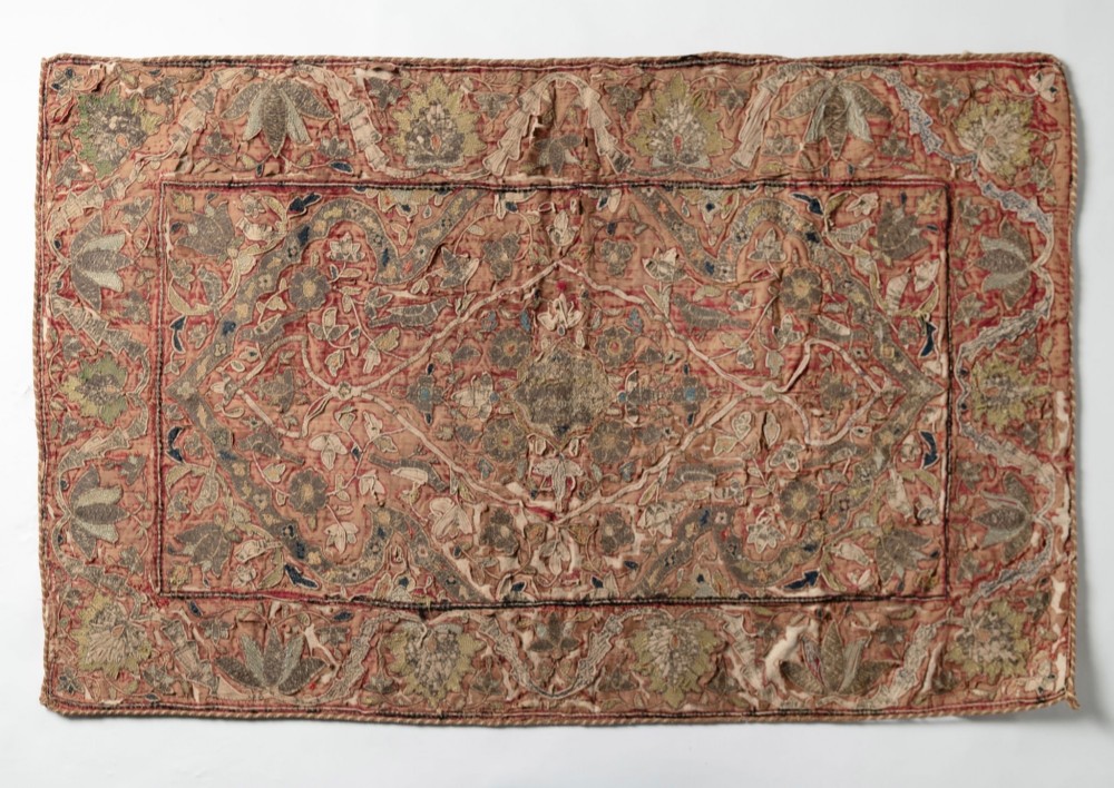A rectangular 18th-century hand-embroidered textile featuring a central diamond medallion with floral arabesques and border patterns in shades of muted pink, sage green, and cream.