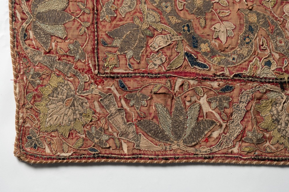 A rectangular 18th-century hand-embroidered textile featuring a central diamond medallion with floral arabesques and border patterns in shades of muted pink, sage green, and cream. View V