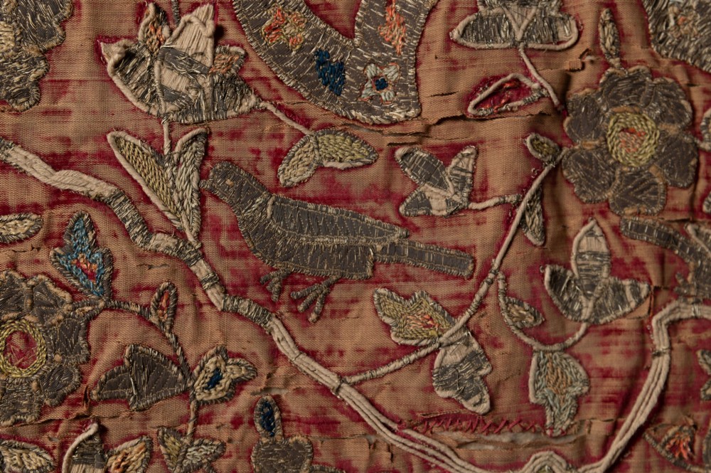 A rectangular 18th-century hand-embroidered textile featuring a central diamond medallion with floral arabesques and border patterns in shades of muted pink, sage green, and cream. View VIII