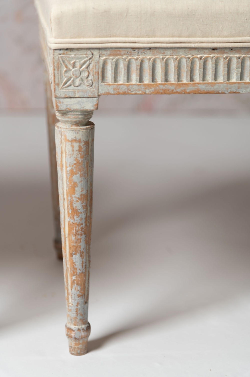 A pair of antique Swedish Gustavian stools featuring distressed pale grey painted wooden frames with fluted legs and cream fabric seats. View II