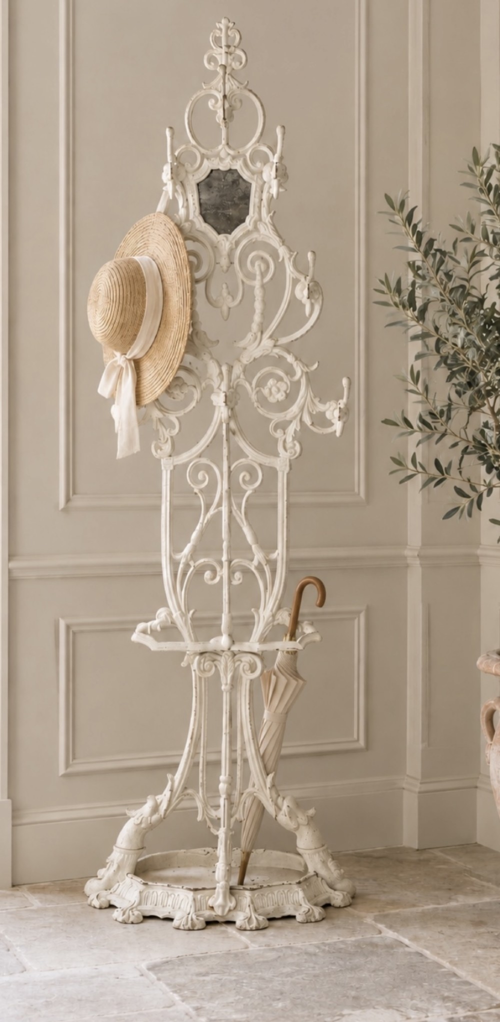 An antique white painted cast iron hall stand featuring intricate scrollwork, integrated coat hooks, a small central mirror, and a base drip tray.