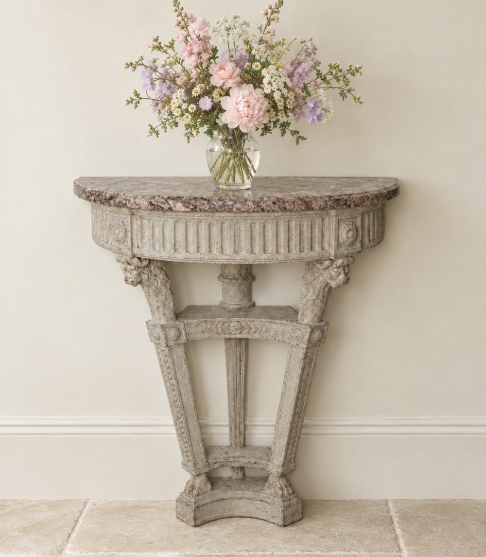 An antique French demilune console table featuring a pink veined marble top over a painted carved frame with lion head motifs.