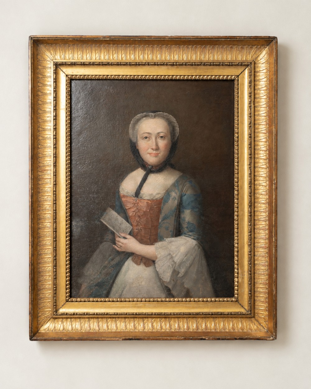 An 18th-century oil painting depicting a seated woman in period dress holding a document, housed in a carved gold giltwood frame.