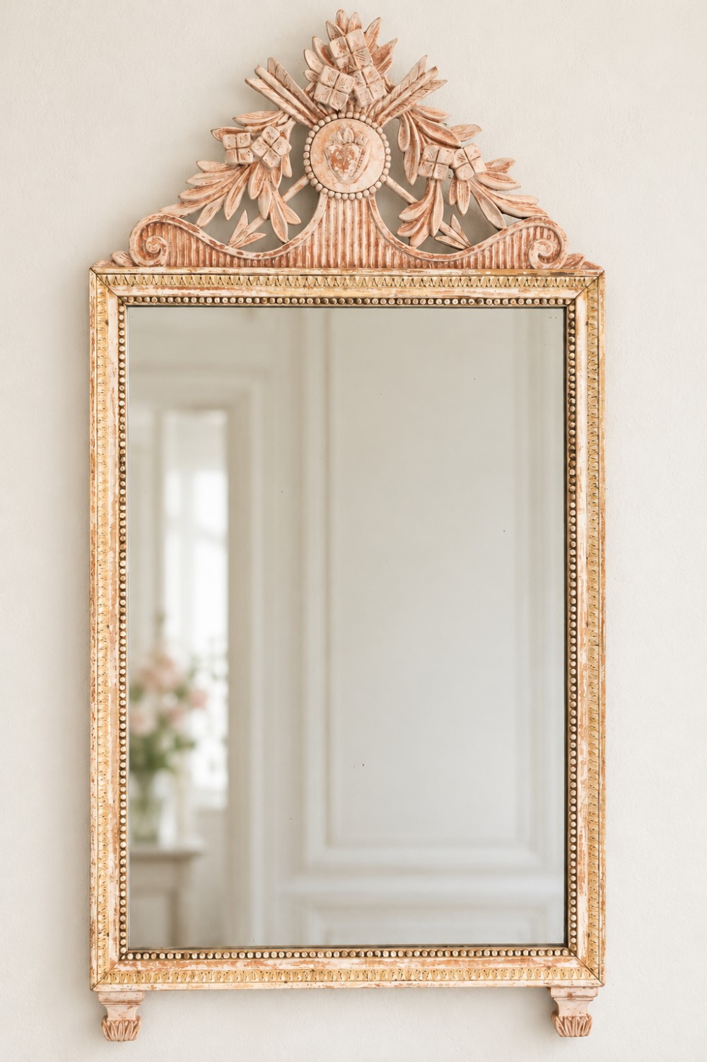 A rectangular antique French wall mirror with a cream painted frame, beaded inner border, and a carved crest pediment featuring floral motifs.