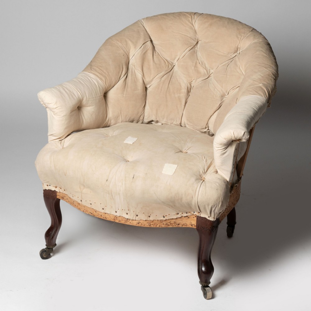 A low-back French armchair featuring cream button-tufted upholstery, carved walnut cabriole front legs, and brass castors.