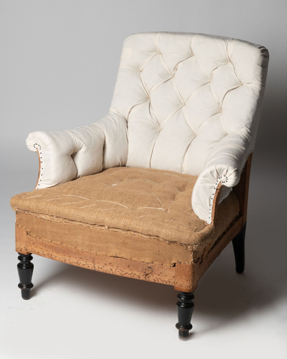 An antique French armchair in calico and hessian lining with deep buttoning and dark turned front legs.
