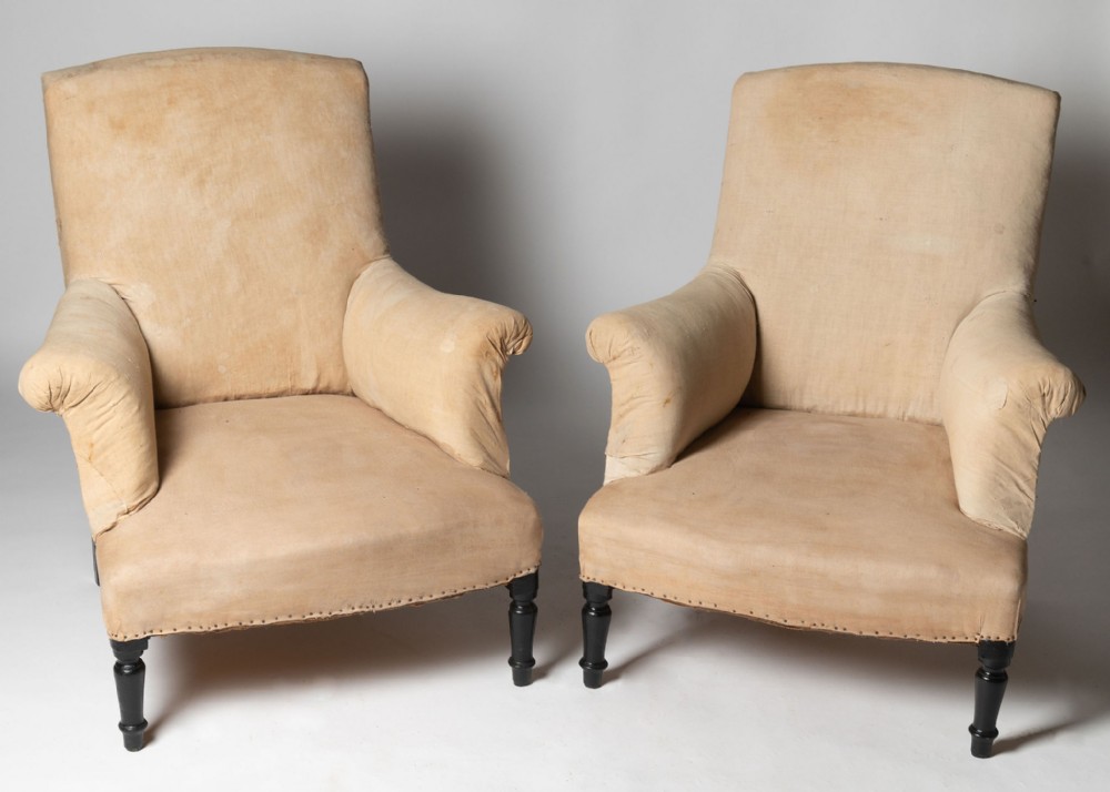 A pair of antique French armchairs upholstered in beige calico fabric with dark turned wood front legs and rolled arms.