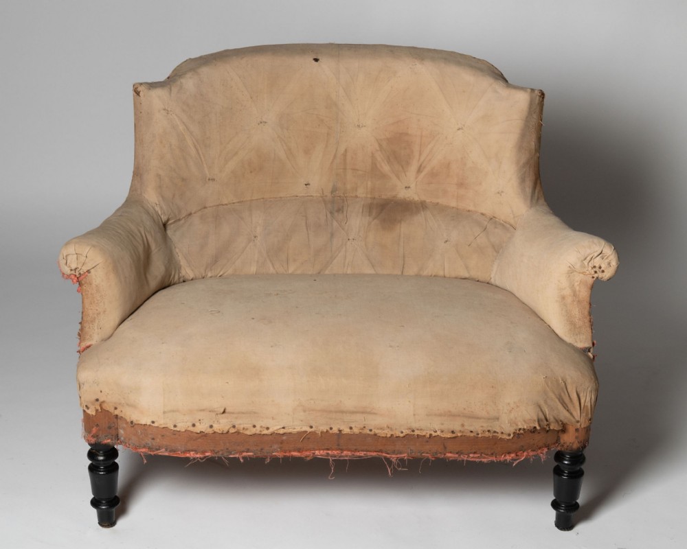 An antique French marquise chair featuring extra wide seating, button-tufted calico lining, and turned ebonised front legs.