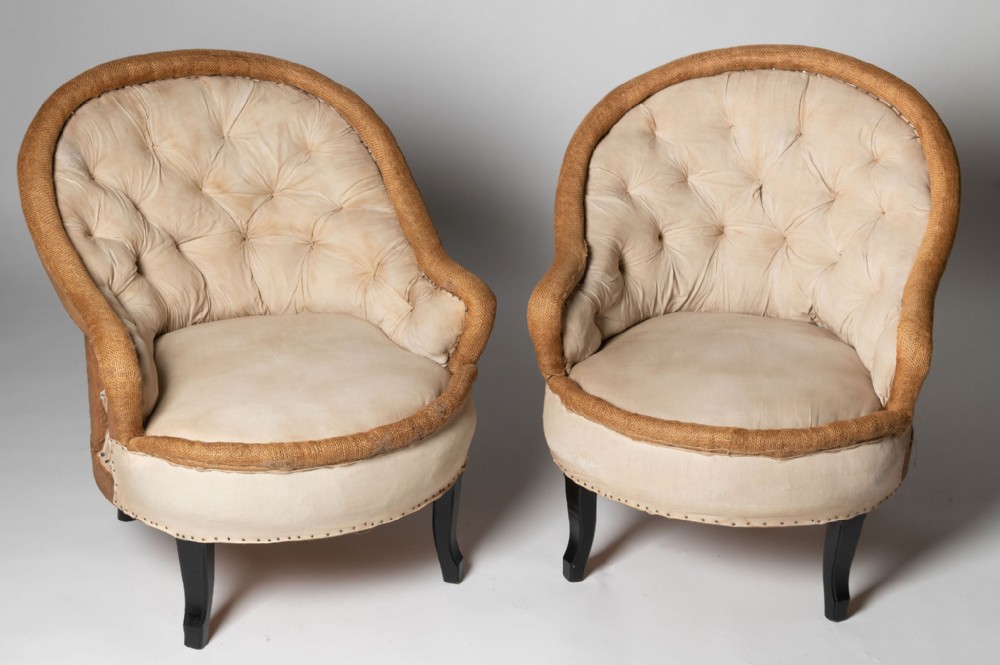 A pair of antique French crapaud armchairs featuring button-tufted cream calico upholstery, exposed hessian edging, and dark ebonised legs.