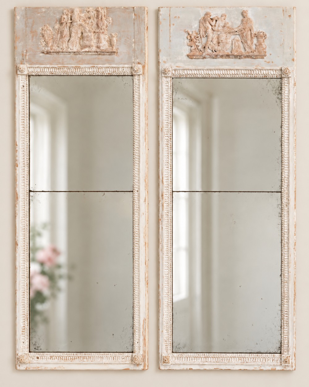 A pair of tall French painted pier mirrors featuring carved classical bas-relief friezes and distressed off-white frames.