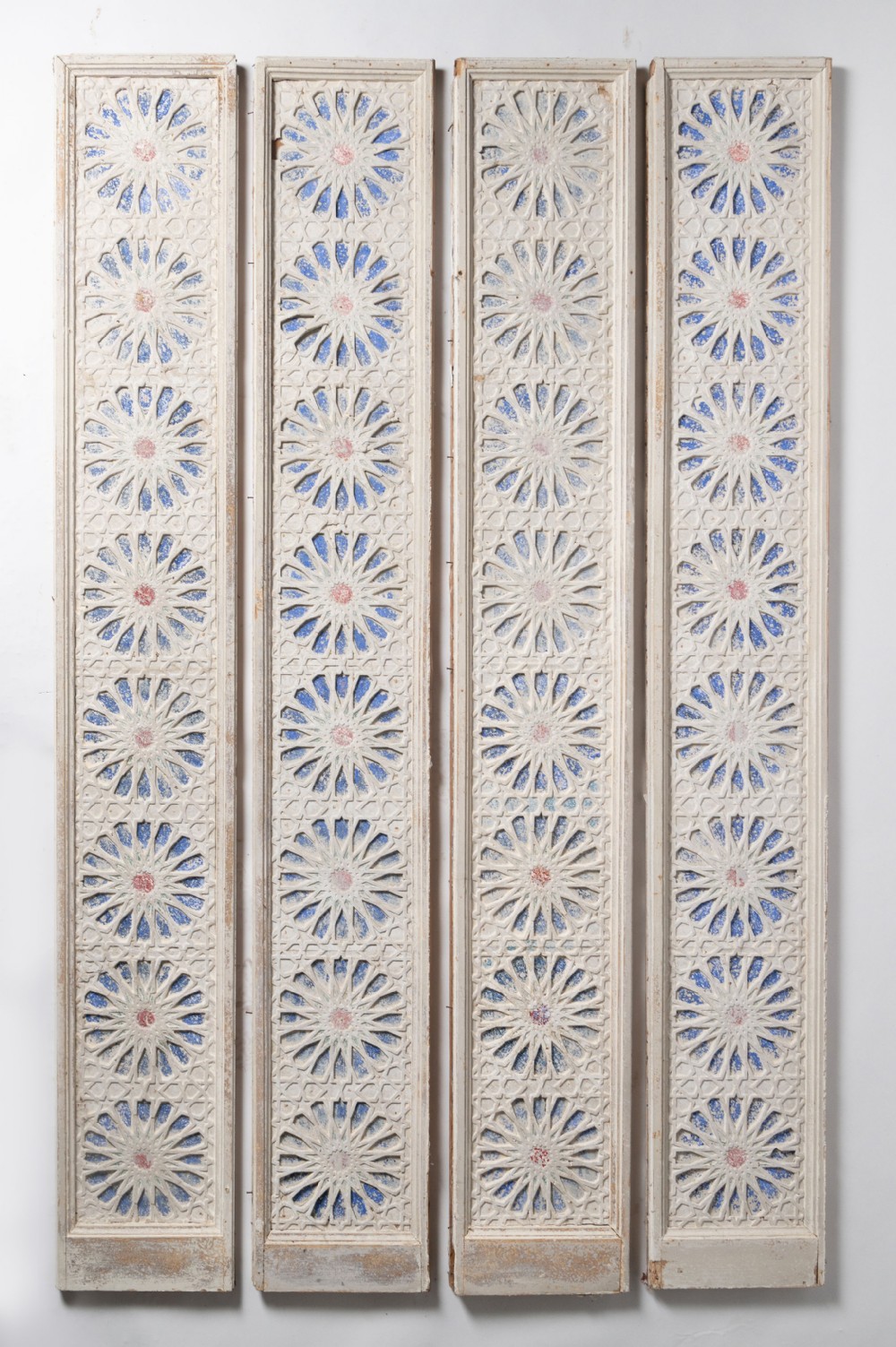 A set of four tall, narrow carved wood architectural panels with geometric star motifs painted in off-white, blue, and red.
