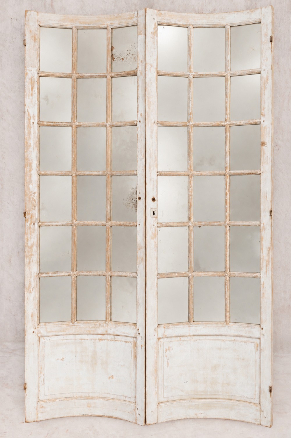 A pair of antique French concave glazed doors featuring distressed off-white painted wooden frames with multiple glass panes and panelled bottoms.