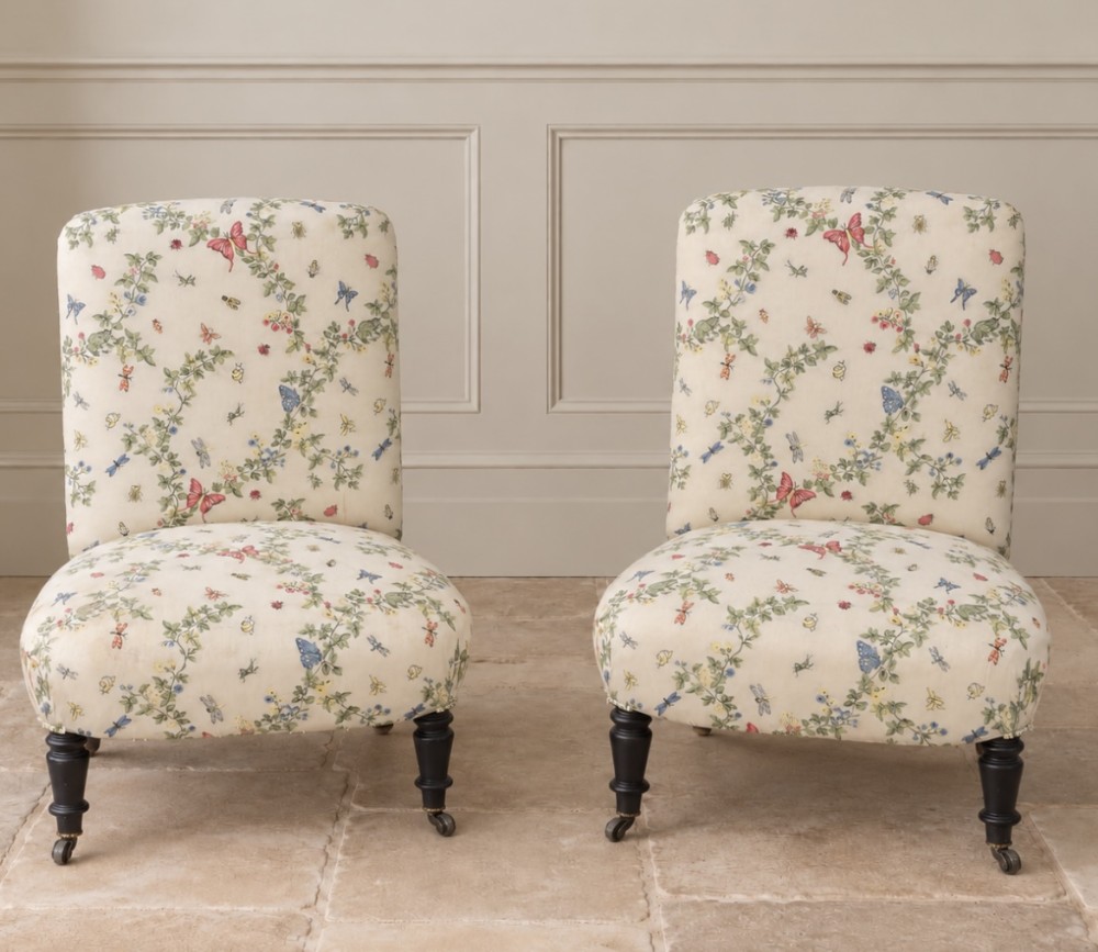A pair of antique Napoleon III armless slipper chairs upholstered in floral botanical fabric with ebonised turned legs and brass castors.