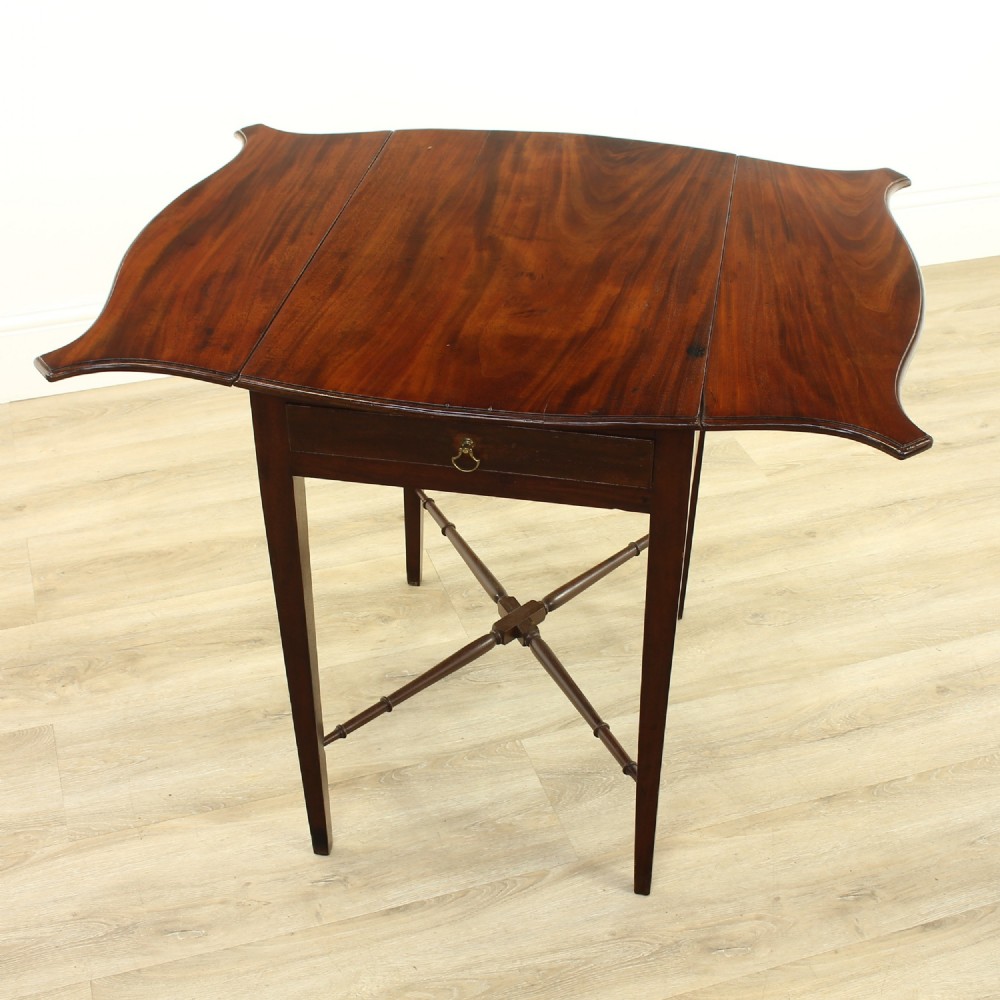 A Georgian mahogany butterfly Pembroke table featuring open shaped drop leaves, a single drawer, tapered square legs, and a turned X-frame stretcher.