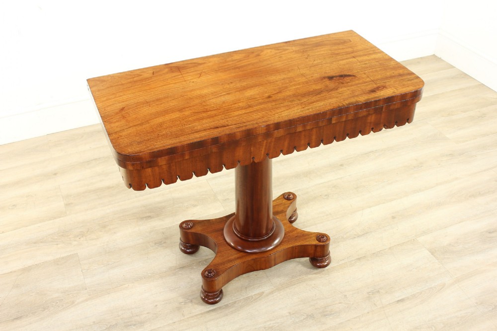 A Georgian satin walnut pedestal tea table featuring a rectangular fold-over top, a scalloped apron, a turned cylindrical column, and a four-pointed plinth base on flattened ball feet.