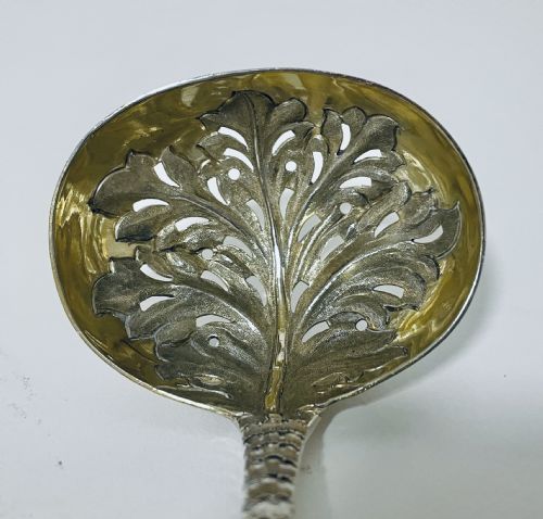 fig 1. A Georgian sterling silver sugar sifter spoon featuring a hand-pierced foliate bowl design and an engraved floral handle.