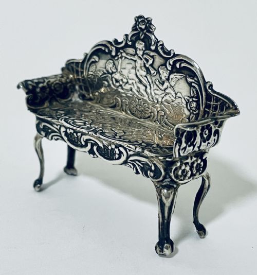 fig 1. An ornate miniature sterling silver sofa featuring embossed cherub motifs, scrollwork backrest, and cabriole legs.