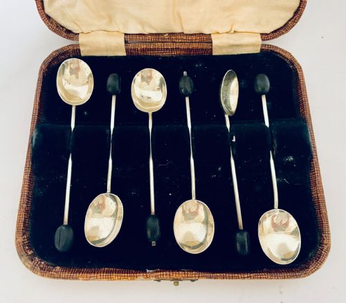 fig 1. A set of six Art Deco silver coffee spoons with dark bean finials presented inside an open velvet-lined brown case.