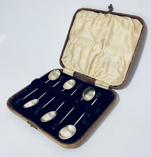 fig 2. A set of six Art Deco silver coffee spoons with dark bean finials presented inside an open velvet-lined brown case.