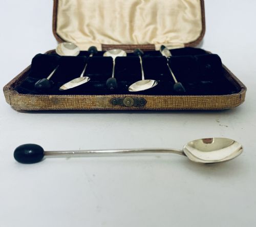 fig 3. A set of six Art Deco silver coffee spoons with dark bean finials presented inside an open velvet-lined brown case.