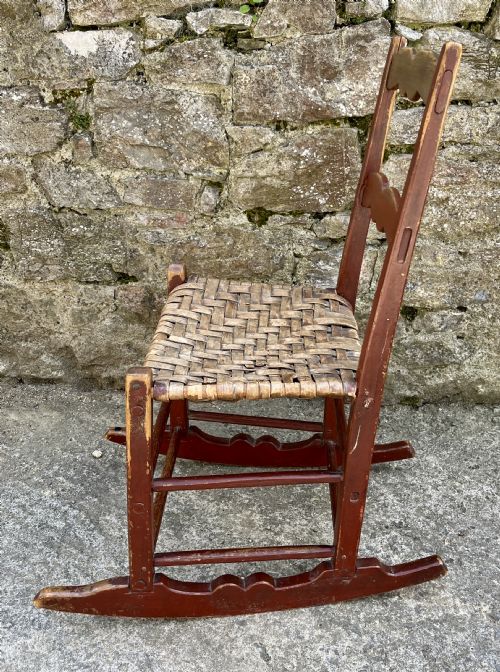 fig 1. A primitive red-painted wooden rocking chair featuring a woven splint seat and scalloped back slats.