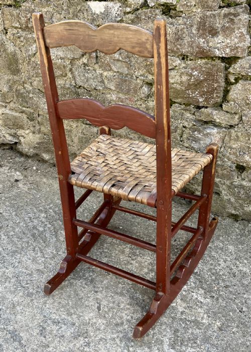 fig 2. A primitive red-painted wooden rocking chair featuring a woven splint seat and scalloped back slats.
