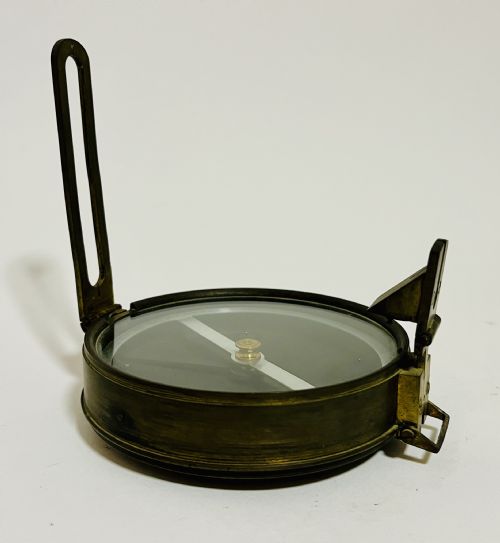 fig 1. An antique brass surveying compass featuring folding sight vanes, a central needle, and a glass-covered dial.