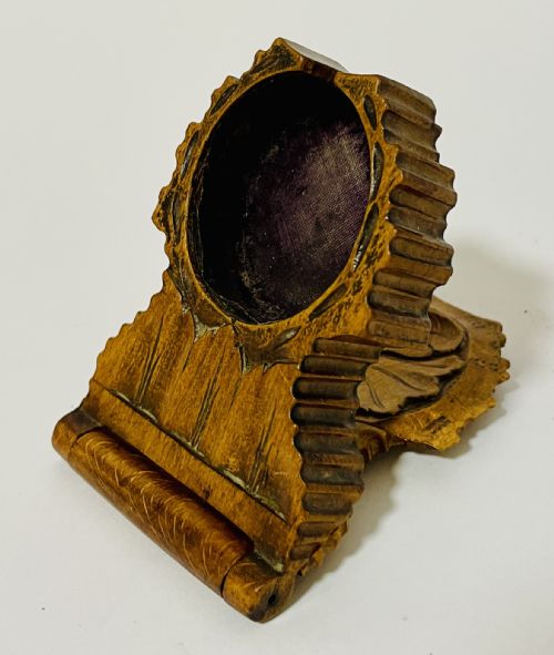 fig 1. An antique carved wooden Black Forest pocket watch holder with leaf detailing on the base and a dark velvet-lined aperture for displaying a timepiece.