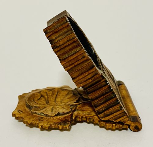 fig 2. An antique carved wooden Black Forest pocket watch holder with leaf detailing on the base and a dark velvet-lined aperture for displaying a timepiece.