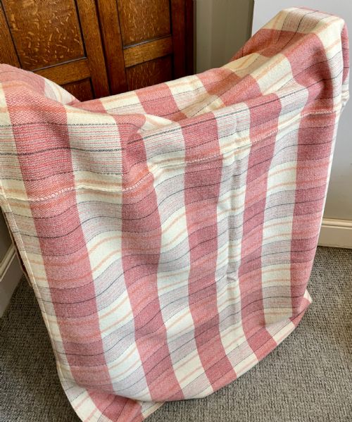 fig 1. A large woven Welsh wool blanket featuring a pink, cream, and subtle yellow plaid grid design.