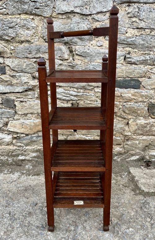 fig 1. A tall, four-tier dark teak ships whatnot stand featuring slatted timber shelves, pyramid finials, a top carrying rail, and a brass makers plaque on the lowest shelf.