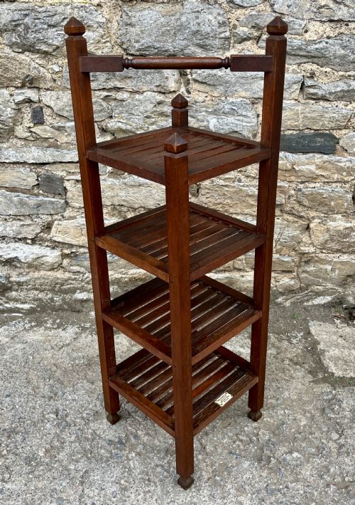 fig 2. A tall, four-tier dark teak ships whatnot stand featuring slatted timber shelves, pyramid finials, a top carrying rail, and a brass makers plaque on the lowest shelf.