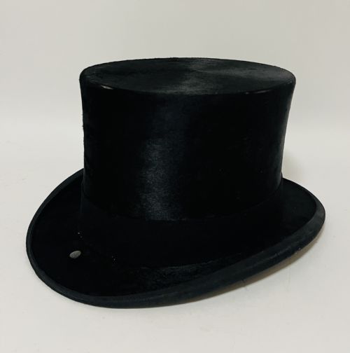 fig 1. A black silk plush top hat resting on top of a bucket-shaped tan leather carrying case with a metal lock.