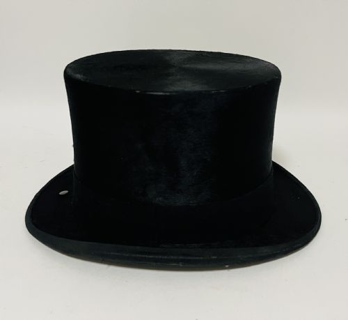 fig 2. A black silk plush top hat resting on top of a bucket-shaped tan leather carrying case with a metal lock.