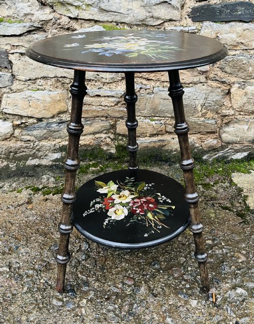 fig 1. A circular two-tiered ebonised wooden side table featuring turned bobbin legs and hand-painted floral arrangements on both levels.