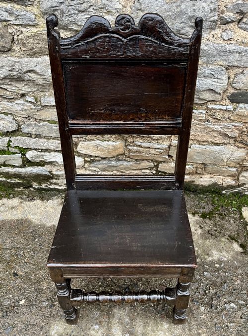 fig 1. A dark oak 17th-century backstool featuring a carved crested top rail, solid wooden seat, turned front legs, and a stretchered base.