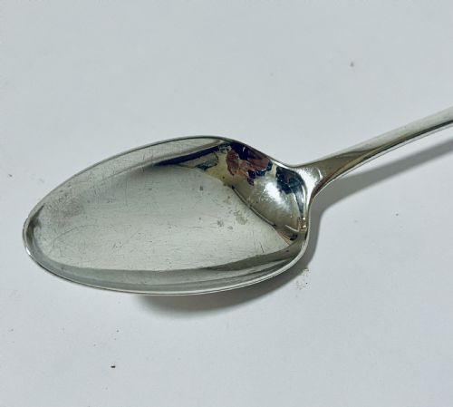 fig 2. An 18th-century sterling silver serving spoon featuring a plain oval bowl and an engraved heraldic crest on the flat handle terminal.