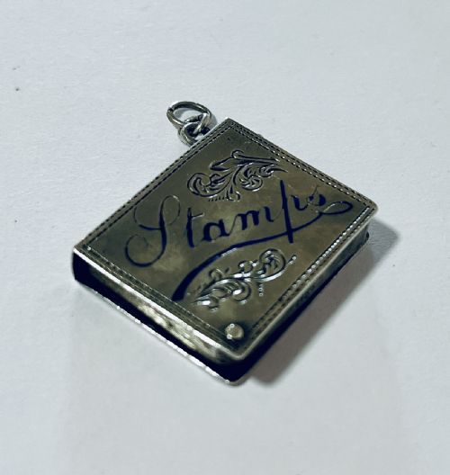 fig 1. An antique silver stamp case featuring engraved foliate scrolls and script lettering with a suspension ring at the top.