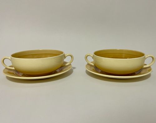 fig 1. A pair of cream glazed earthenware soup coupes with twin handles and matching saucers decorated with ochre yellow, brown, and orange horizontal bands.
