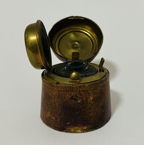 fig 1. A 19th-century Victorian travelling inkwell encased in textured brown leather with a hinged brass lid open to reveal the interior stopper mechanism.