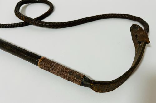 fig 1. An antique hunting whip featuring a carved staghorn handle, a polished silver collar, a dark brown shaft, and a braided leather thong.