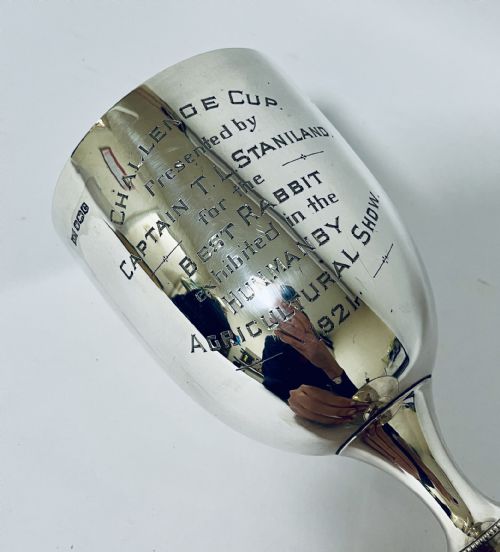 fig 1. An engraved 1921 silver trophy cup featuring a goblet-shaped bowl, knopped stem, circular flared base, and hallmarked upper rim.