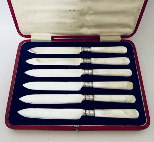 fig 1. A set of six antique silver dessert knives with iridescent mother-of-pearl handles presented inside an open red velvet-lined presentation case.