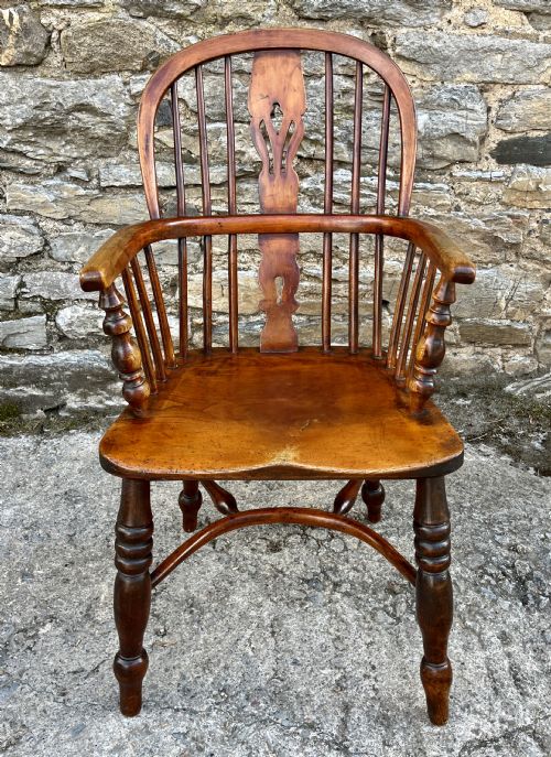 fig 1. A warm brown wooden Windsor armchair featuring a curved hoop back, central pierced splat, turned spindles, shaped armrests, turned legs, and a crinoline stretcher.