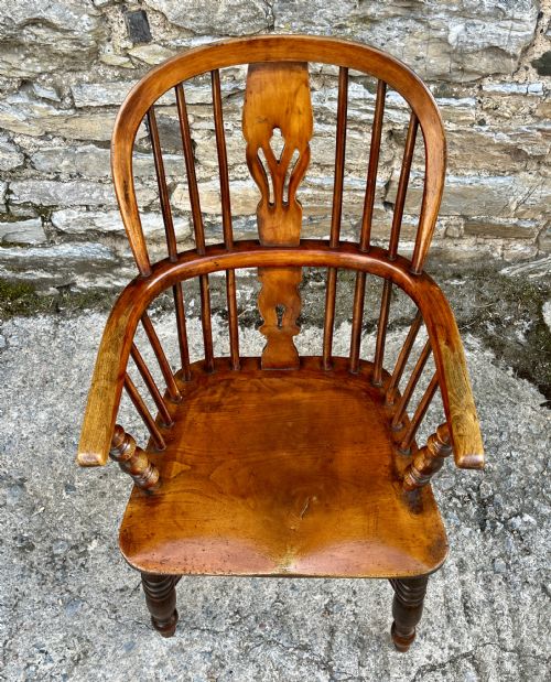 fig 2. A warm brown wooden Windsor armchair featuring a curved hoop back, central pierced splat, turned spindles, shaped armrests, turned legs, and a crinoline stretcher.