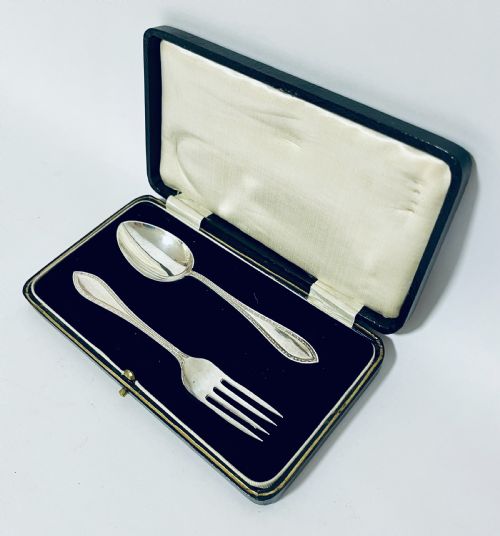 fig 1. An antique silver christening spoon and fork set presented inside an open black fitted case lined with cream silk and dark velvet.